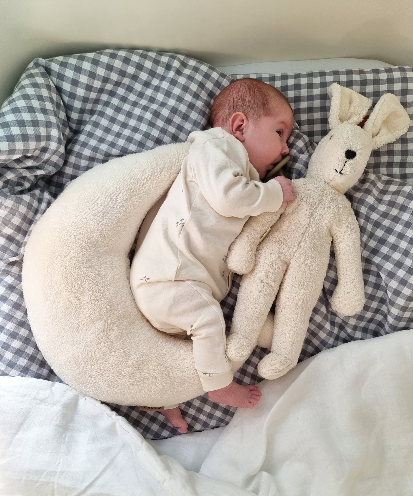 A small baby laying next to a white Senger Small Floppy Rabbit.