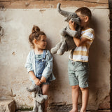 Children holding a large and small Senger cuddly elephant soft toy, standing against a concrete wall
