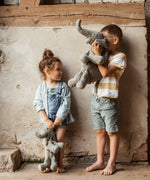 Children holding a large and small Senger cuddly elephant soft toy, standing against a concrete wall