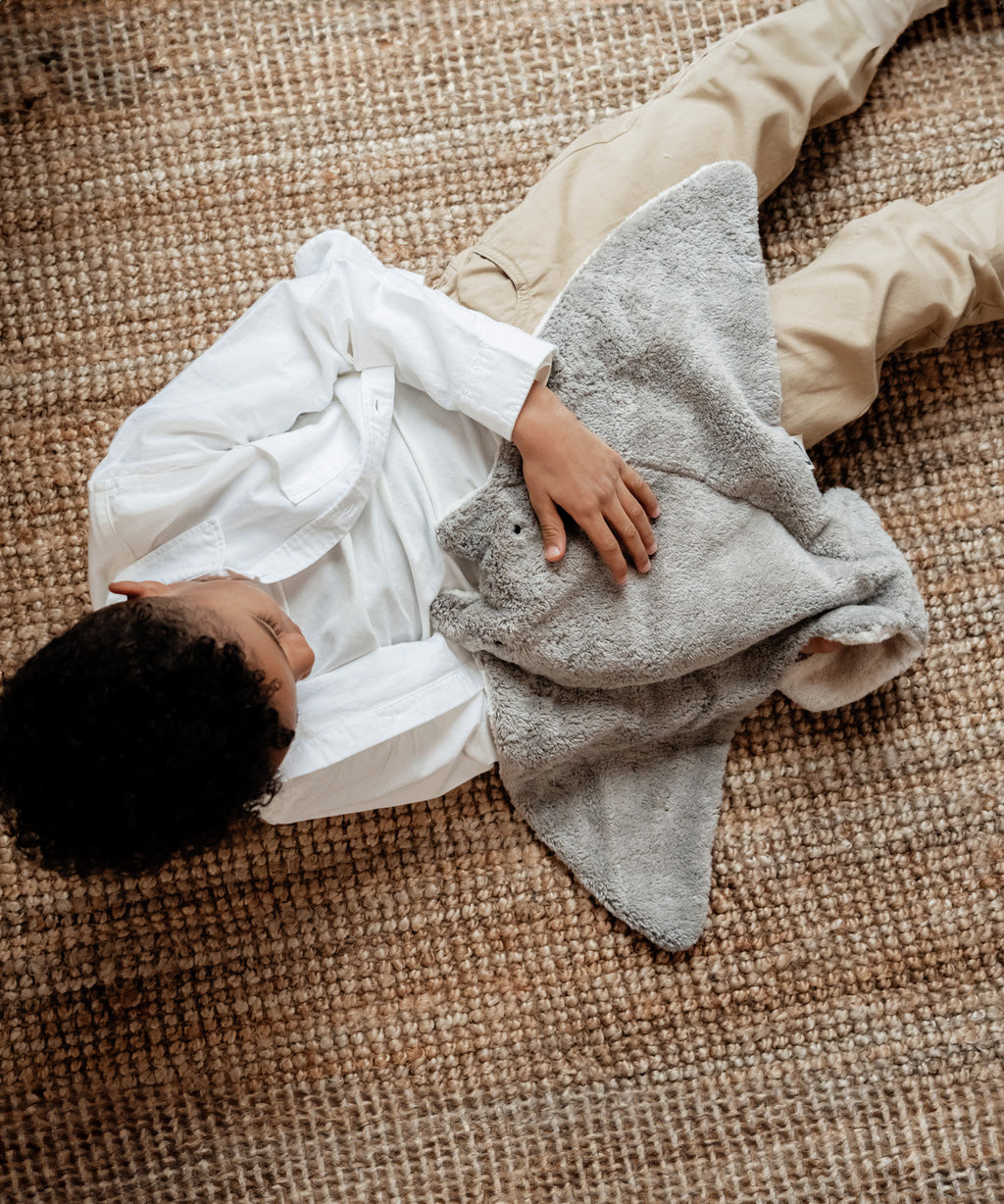 A view looking down on a little boy, cuddling the Senger large organic cotton grey manta ray heatable cuddly toy