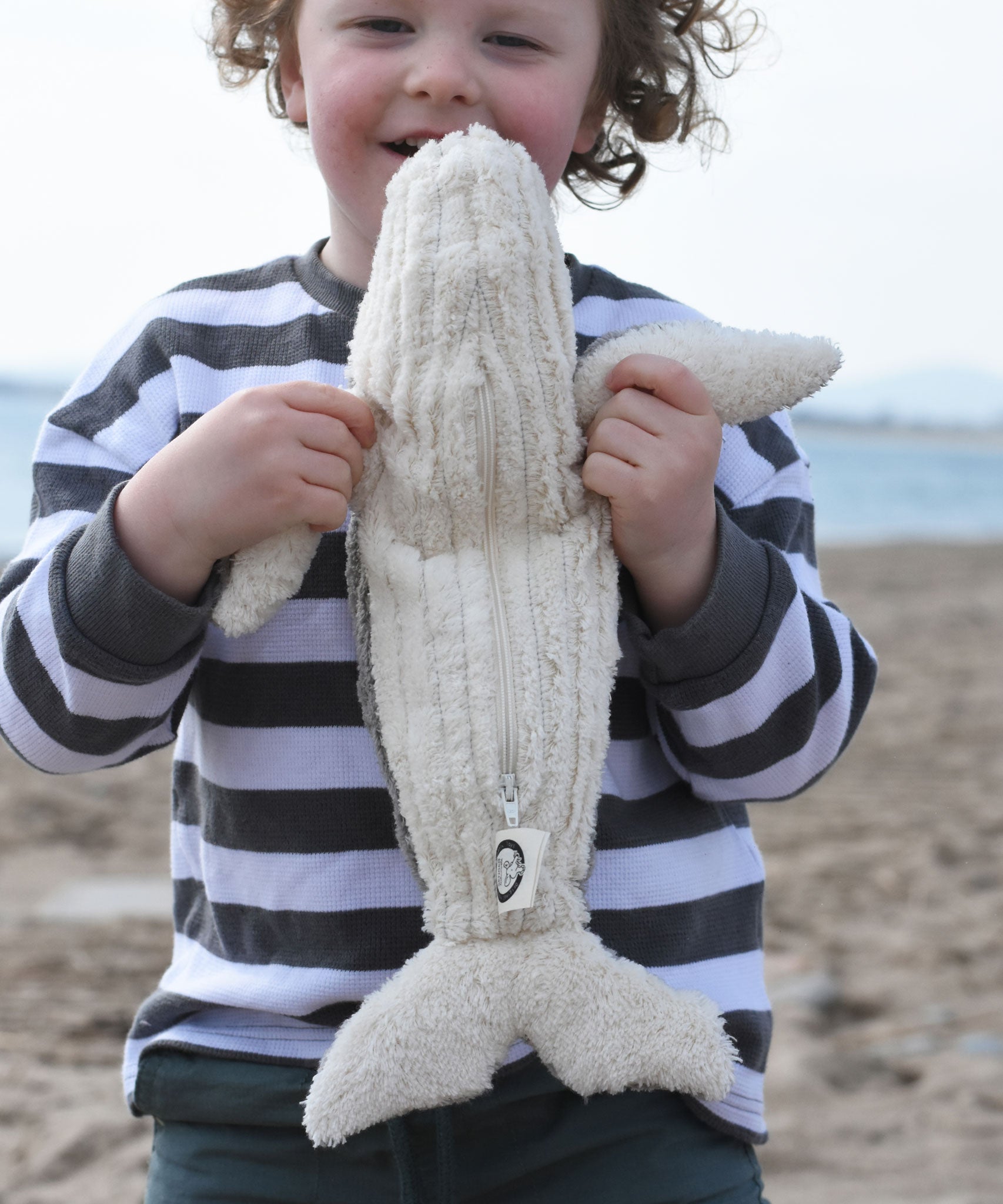A child holding up the small Senger cuddly whale showing the white underside of the whale.