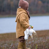Child with a Senge small white goose cuddly toy in their hand. Standing on a grassy surface and a river in the background