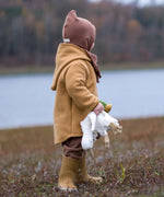 Child with a Senge small white goose cuddly toy in their hand. Standing on a grassy surface and a river in the background