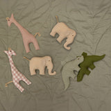 A group of soft grasping toys from Senger available at Babipur on a soft green blanket showing the pink giraffe, beige/cream elephant and the green/plaid stegosaurus soft toys.