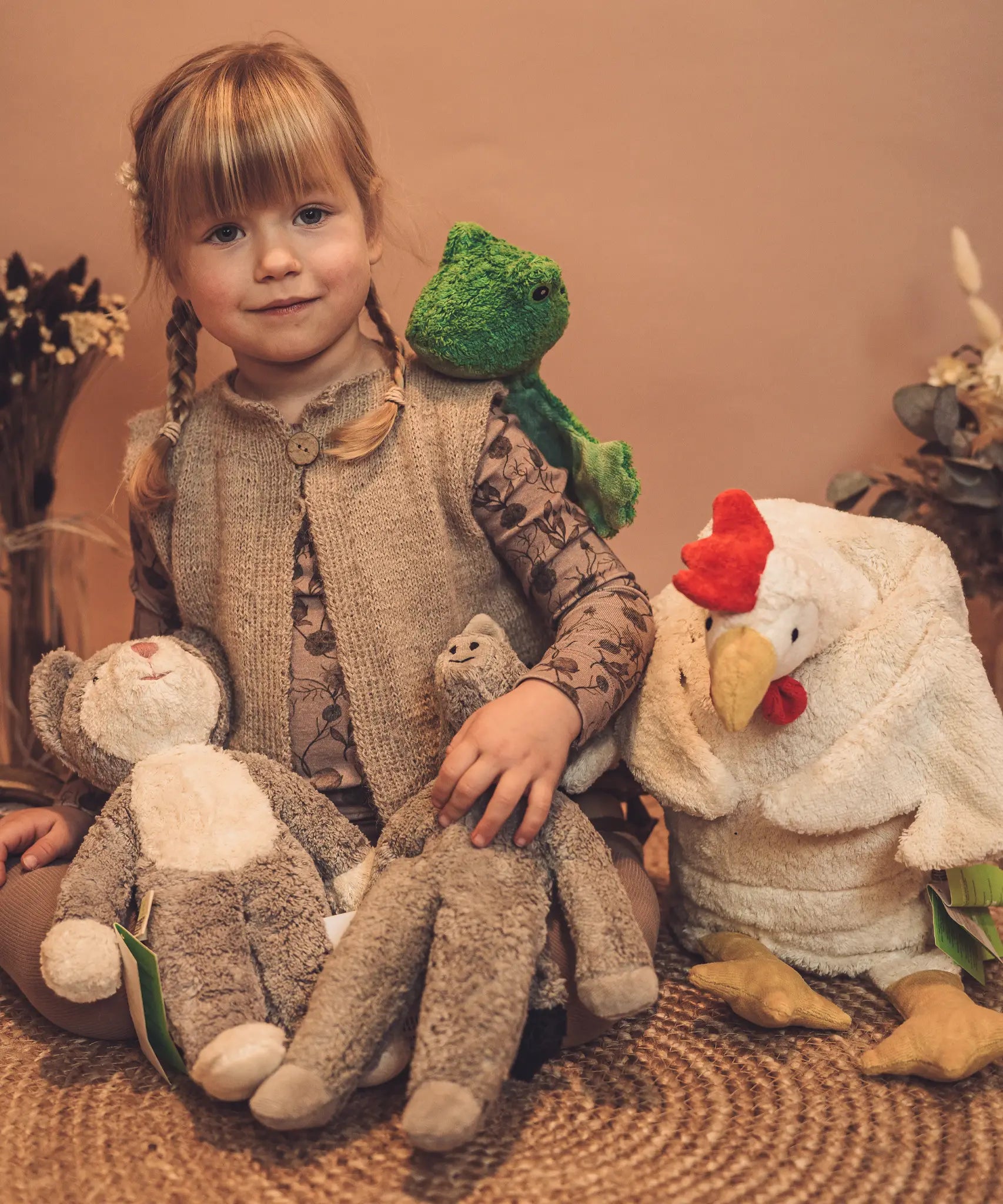 Child sitting next to a Senger baby cat, frog, elephant and a large cuddly chicken toy. 