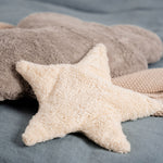 A light yellow, star shaped warming cushion from Senger placed on a  bed with a grey cloud cushion.