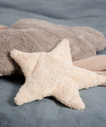 A light yellow, star shaped warming cushion from Senger placed on a  bed with a grey cloud cushion.