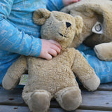 A close up of a small Senger beige cuddly teddy bear in a child's hand.