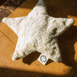 A  Senger light yellow coloured star shaped warming cushion placed on a wooden surface. 