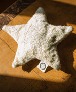 A  Senger light yellow coloured star shaped warming cushion placed on a wooden surface. 