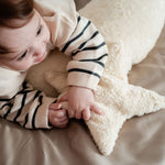 A young child laying besides a Senger light yellow, star shaped warming cushion.