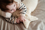 A young child laying besides a Senger light yellow, star shaped warming cushion.
