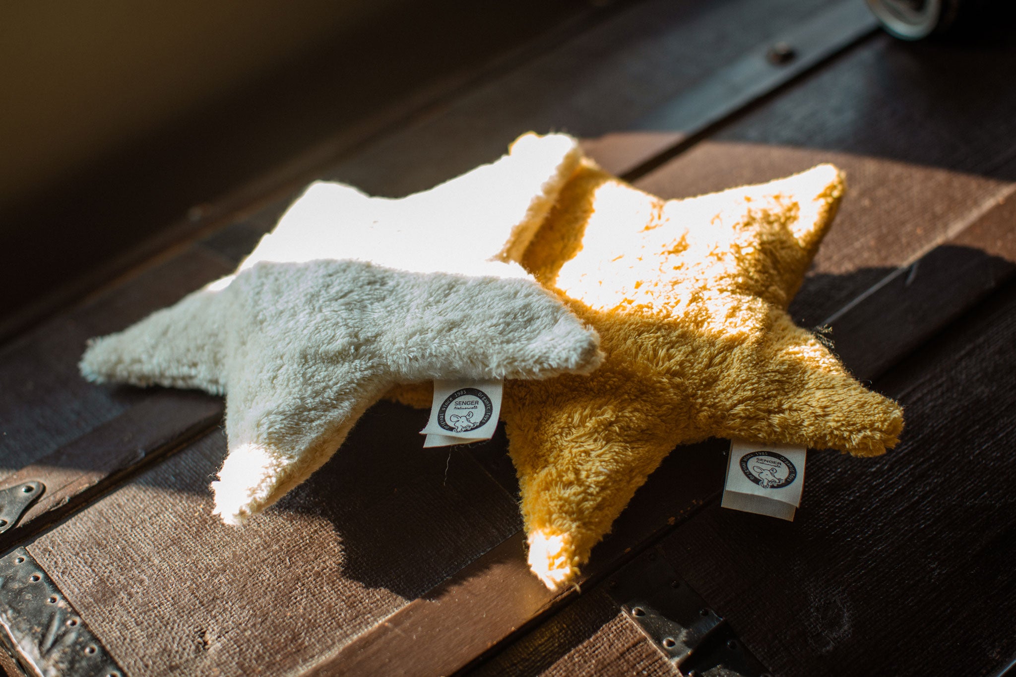 Two Senger star shaped warming cushions placed on the top of a trunk. One is a light yellow, off white colour and the other is a bright yellow colour. 