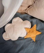 A yellow Senger star shaped warming cushion placed on a bed next to a white cloud cushion.
