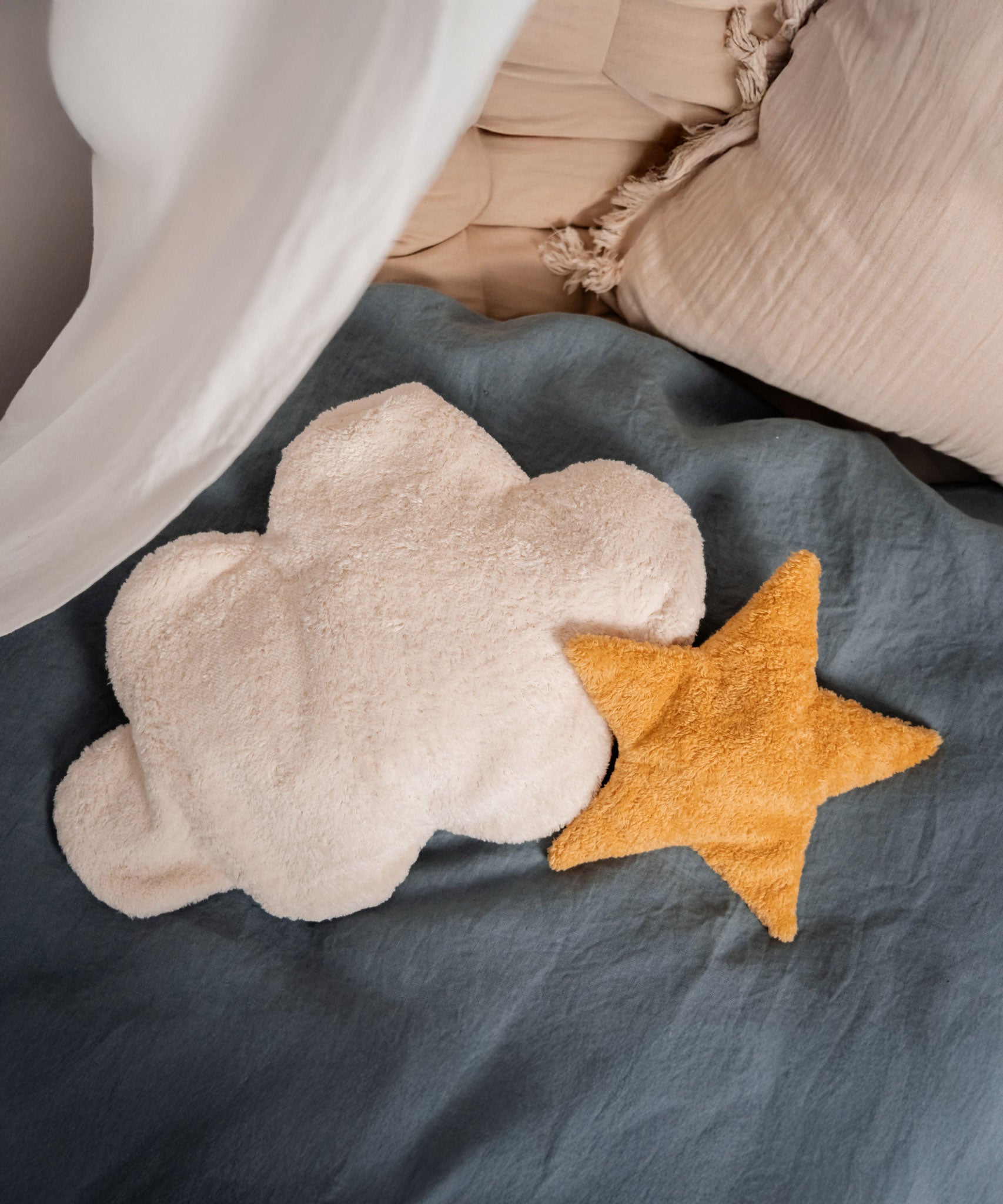 A yellow Senger star shaped warming cushion placed on a bed next to a white cloud cushion.
