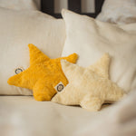 Two Senger star shaped warming cushions placed on a bed. One is a light yellow, off white colour and the other is a bright yellow colour. 
