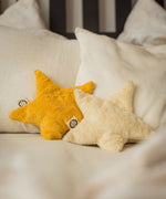 Two Senger star shaped warming cushions placed on a bed. One is a light yellow, off white colour and the other is a bright yellow colour. 