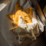 Two Senger star shaped warming cushions placed on a bed. One is a light yellow, off white colour and the other is a bright yellow colour. 