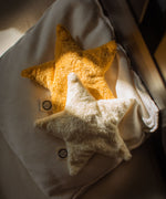 Two Senger star shaped warming cushions placed on a bed. One is a light yellow, off white colour and the other is a bright yellow colour. 