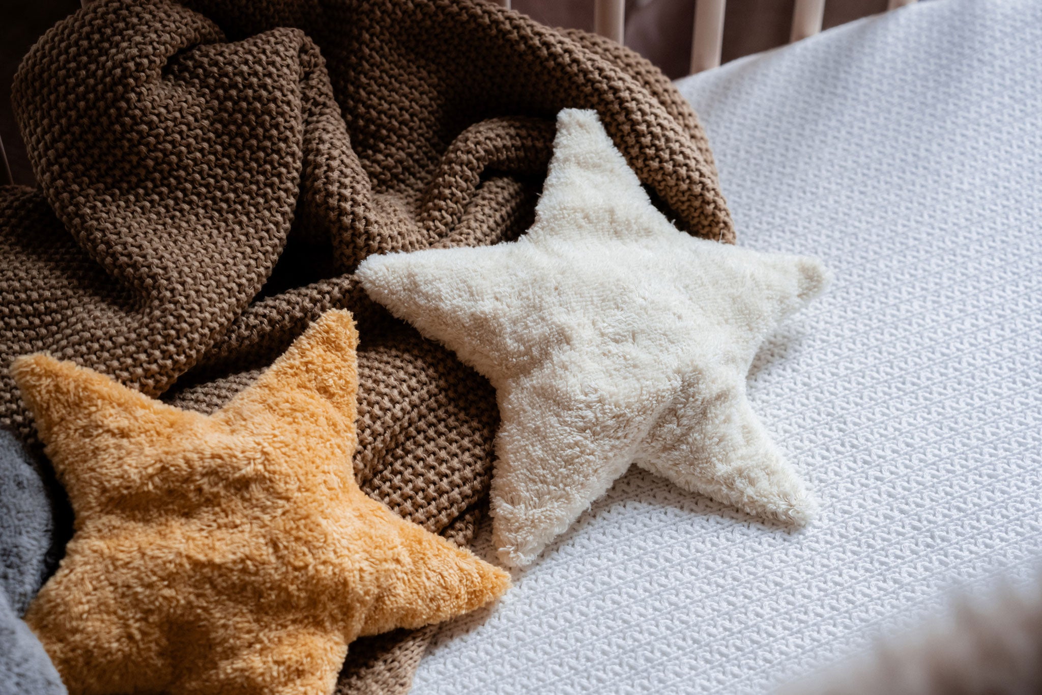 Two Senger star shaped warming cushions placed on a bed on a brown coloured blanket. One is a light yellow, off white colour and the other is a bright yellow colour. 