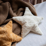 Two Senger star shaped warming cushions placed on a bed on a brown coloured blanket. One is a light yellow, off white colour and the other is a bright yellow colour. 