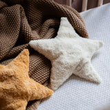 Two Senger star shaped warming cushions placed on a bed on a brown coloured blanket. One is a light yellow, off white colour and the other is a bright yellow colour. 