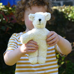 A child holding up a Senger white baby bear organic teddy. 