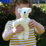 A child holding up a Senger white baby bear organic teddy. 