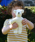 A child holding up a Senger white baby bear organic teddy. 