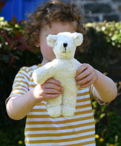 A child holding up a Senger white baby bear organic teddy. 