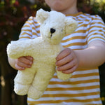 A child holding up a Senger white baby bear organic teddy. 