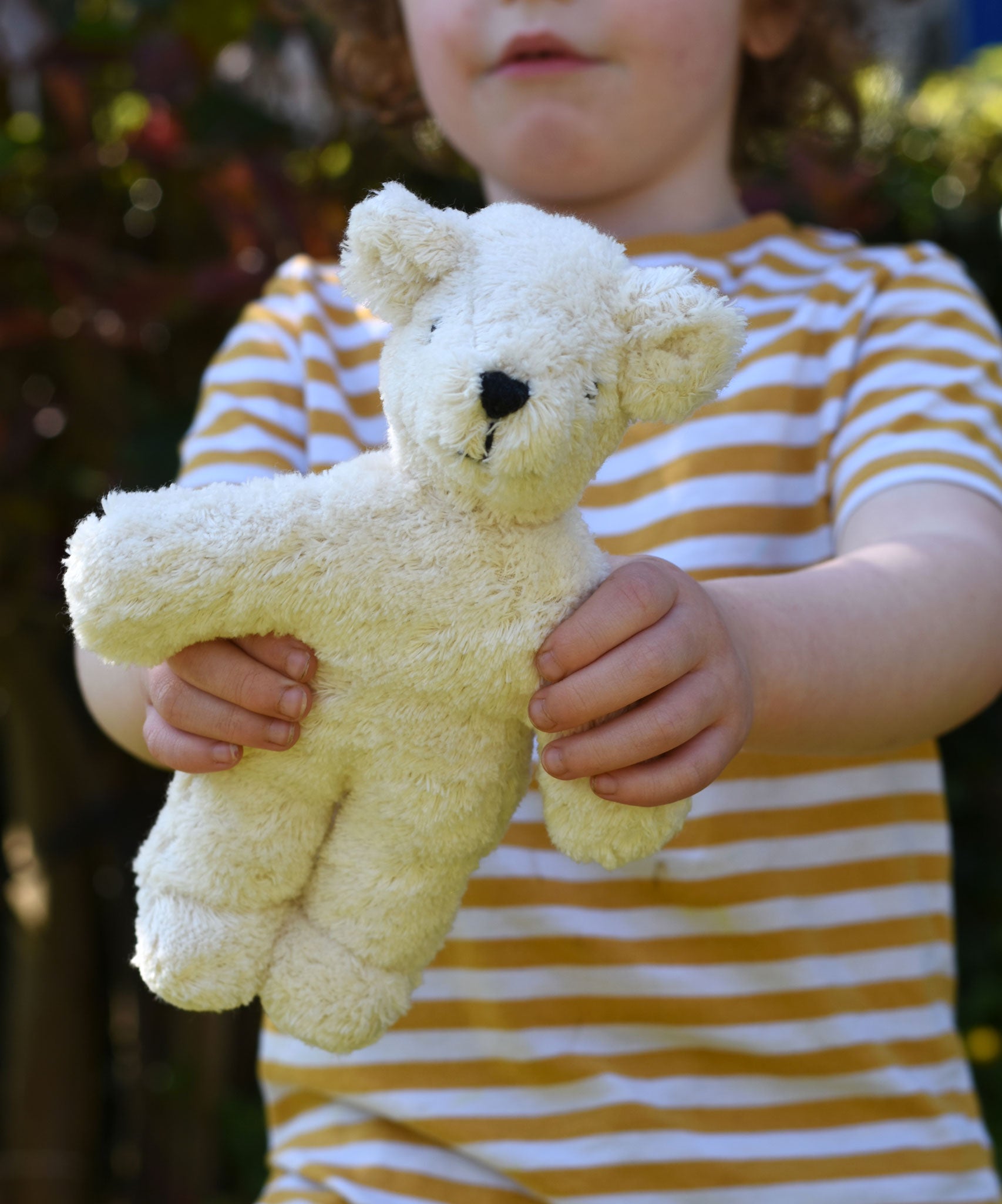 A child holding up a Senger white baby bear organic teddy. 