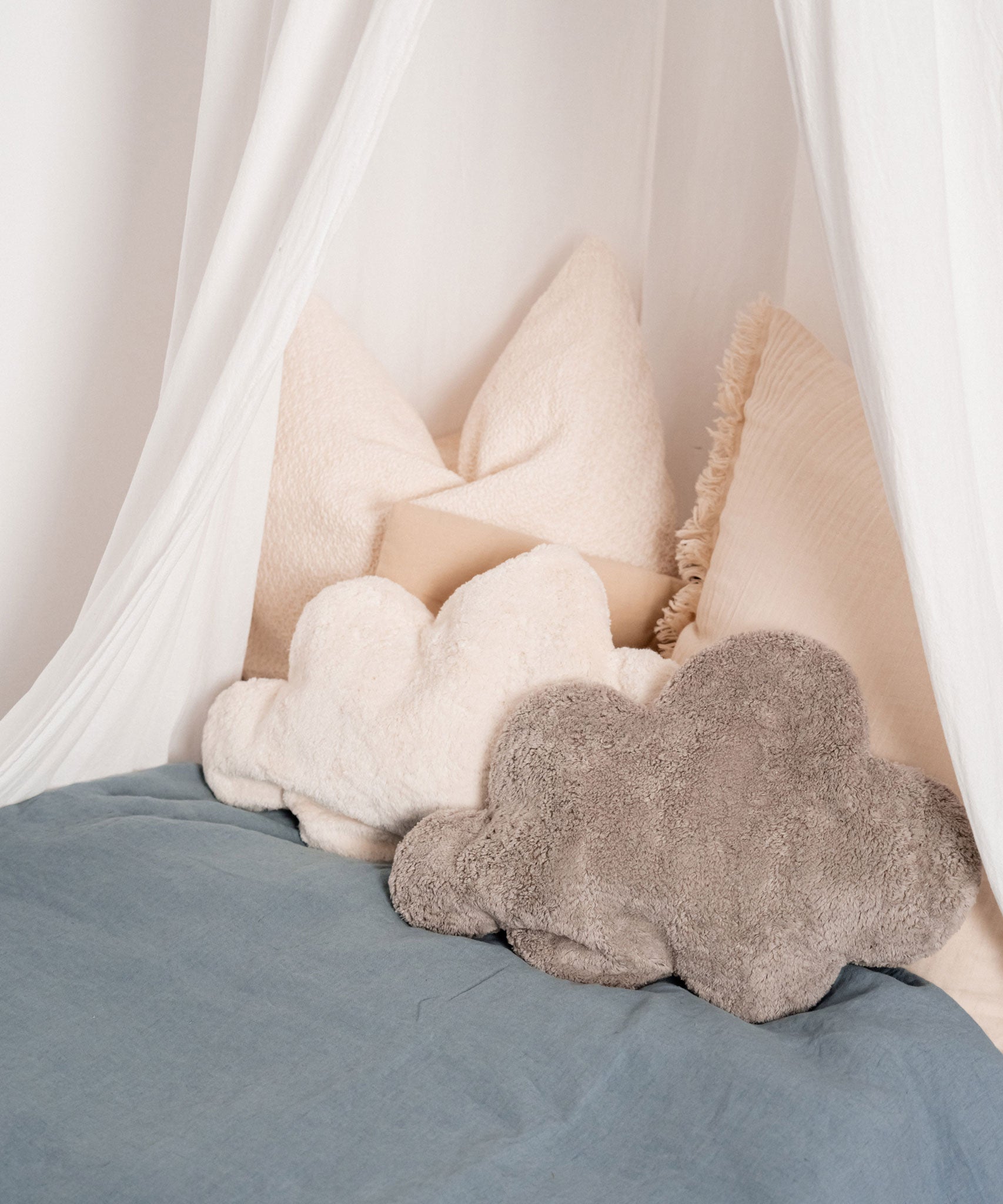 A white and grey cloud shaped Senger warming cushions placed on a bed. 