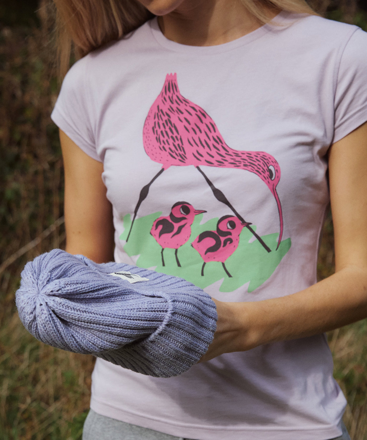 A close up of a woman wearing the Silverstick Matt Sewell Curlew Organic T-Shirt in a Lilac colour way.