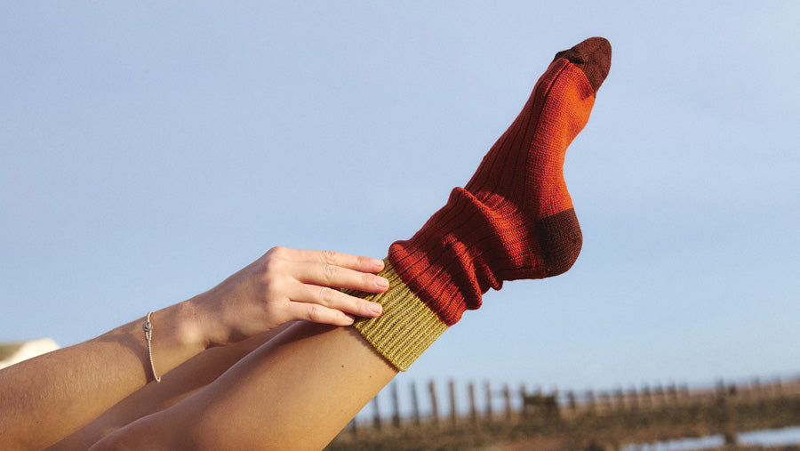 A closeup of a woman's foot stretched to the sky, wearing a red Silverstick Merino wool sock.