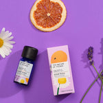 Sleep Well pure essential oil blend in a blue glass bottle next to a decorative pink cardboard box, chamomile flower, lavender flower and orange slice on a purple background. 