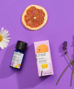 Sleep Well pure essential oil blend in a blue glass bottle next to a decorative pink cardboard box, chamomile flower, lavender flower and orange slice on a purple background. 