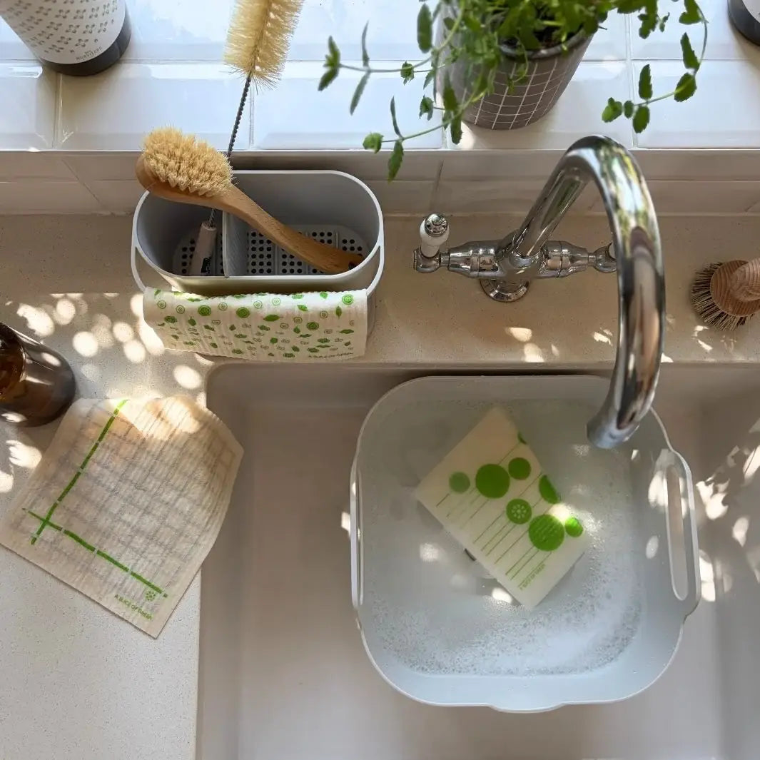 Reusable Mint Leaf Swedish sponge cloths being washed and dried around a kitchen sink for repeated use in a plastic-free home.