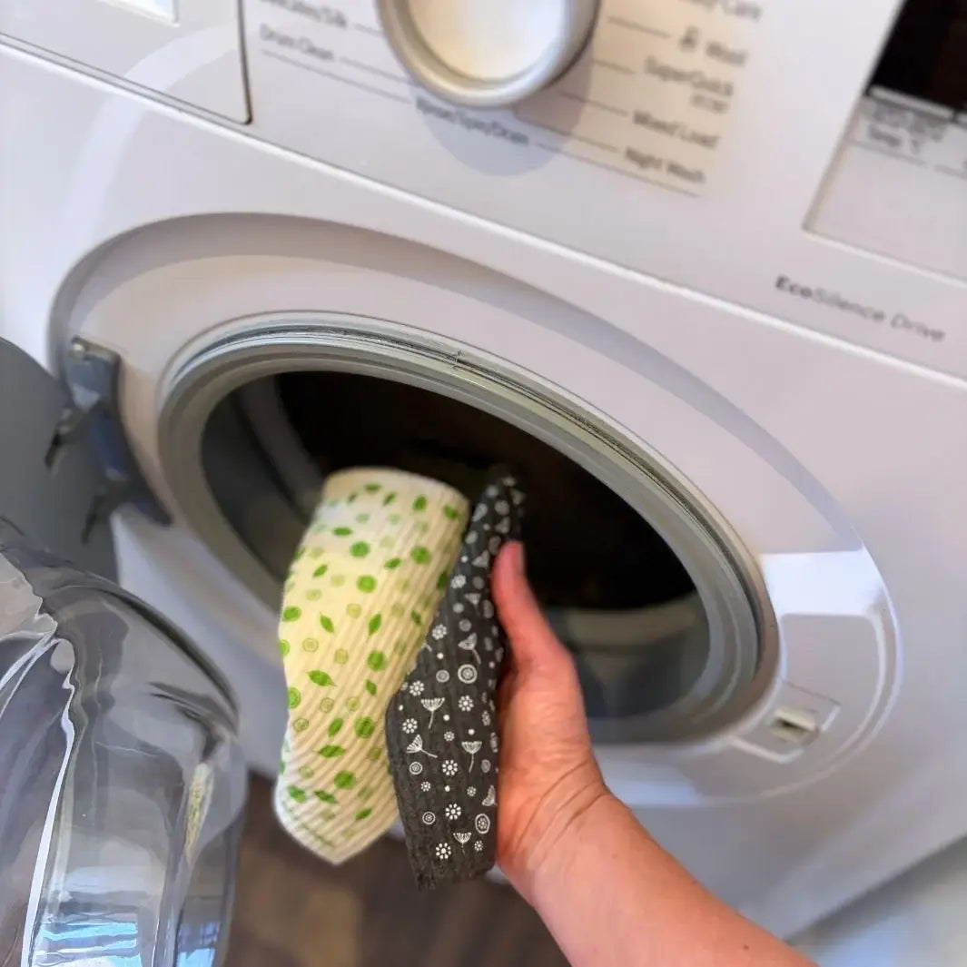 A Slice of Green natural material Swedish sponge cloths being put in a washing machine, showing that the reusable cloths are machine washable.