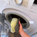 A Slice of Green natural material Swedish sponge cloths being put in a washing machine, showing that the reusable cloths are machine washable.