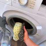A Slice of Green natural material Swedish sponge cloths being put in a washing machine, showing that the reusable cloths are machine washable.