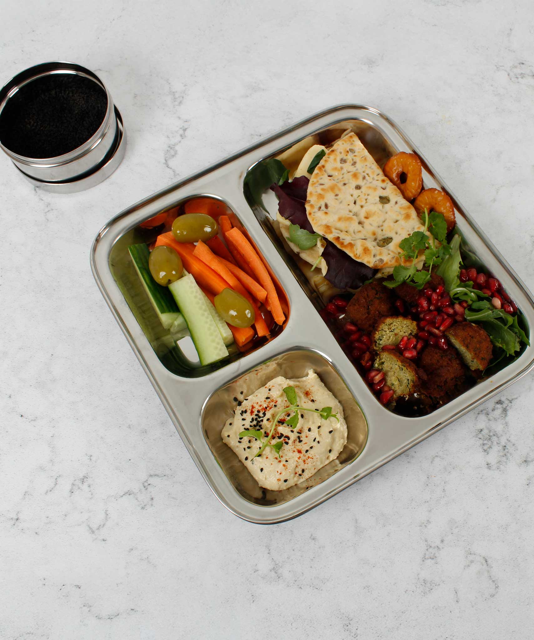 A Slice Of Green Stainless Steel Divided Plate. The plate has hummus in the smallest section, carrot, cucumber and olives in the middle section and flatbread, salad and falafels in the biggest section. This stainless steel plate is suitable for snacks and meals and perfect for children and adults. 