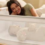 A woman watching over her baby from bed, with the SnuzPod5 close to her bedside.