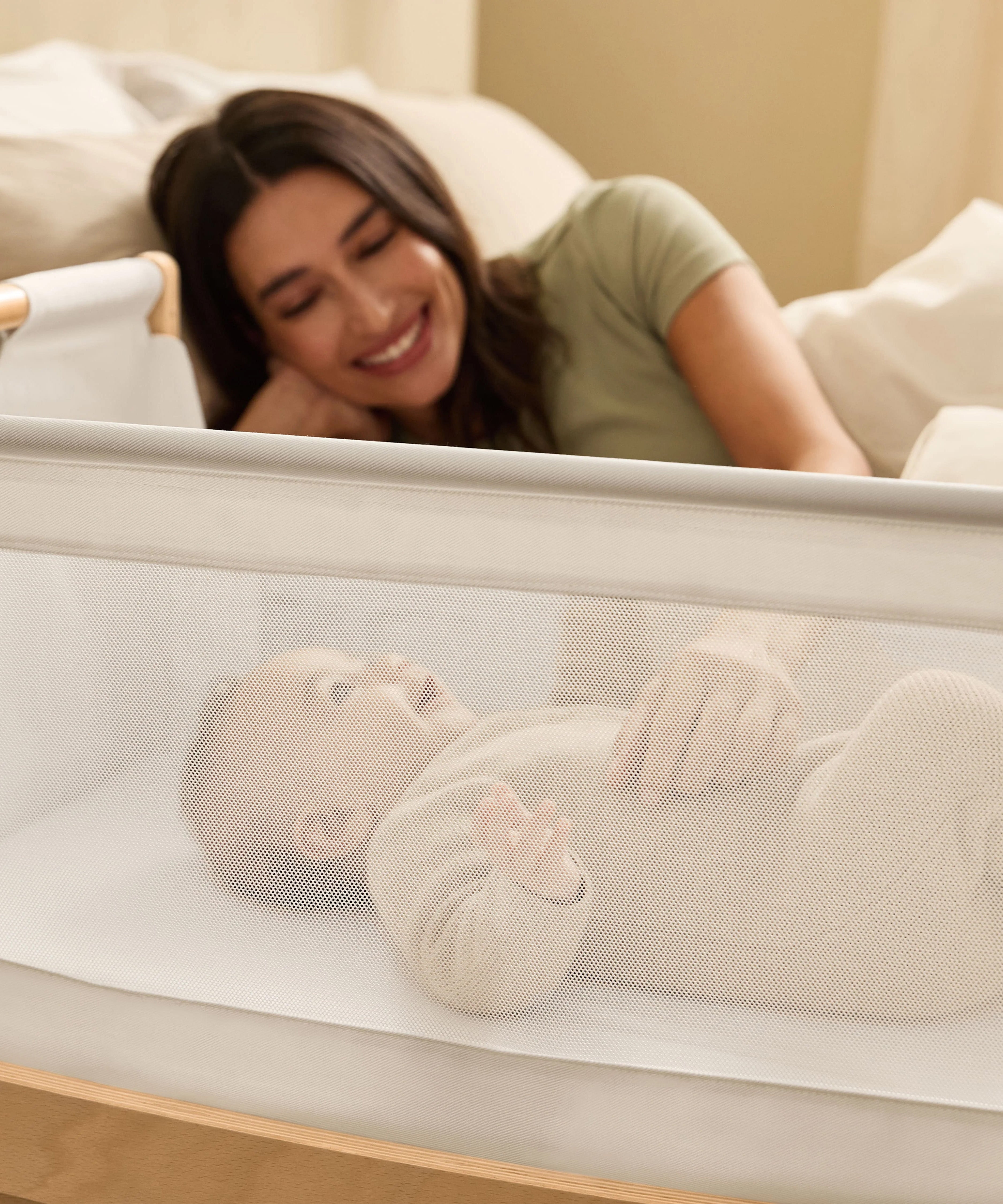 A woman watching over her baby from bed, with the SnuzPod5 close to her bedside.