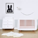 A rose gold SnuzKot pictured in a nursery pictured next to a changing unit