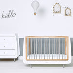 SnuzKot Skandi Cot Bed in grey with a mathcing changing table in a nursery. The nursery has white and grey coloured walls decorated with wooden house shaped shelving 