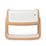 The SnuzPod5 bedside baby crib with a natural, unpainted wooden frame, white mesh sides, and a white mattress. 