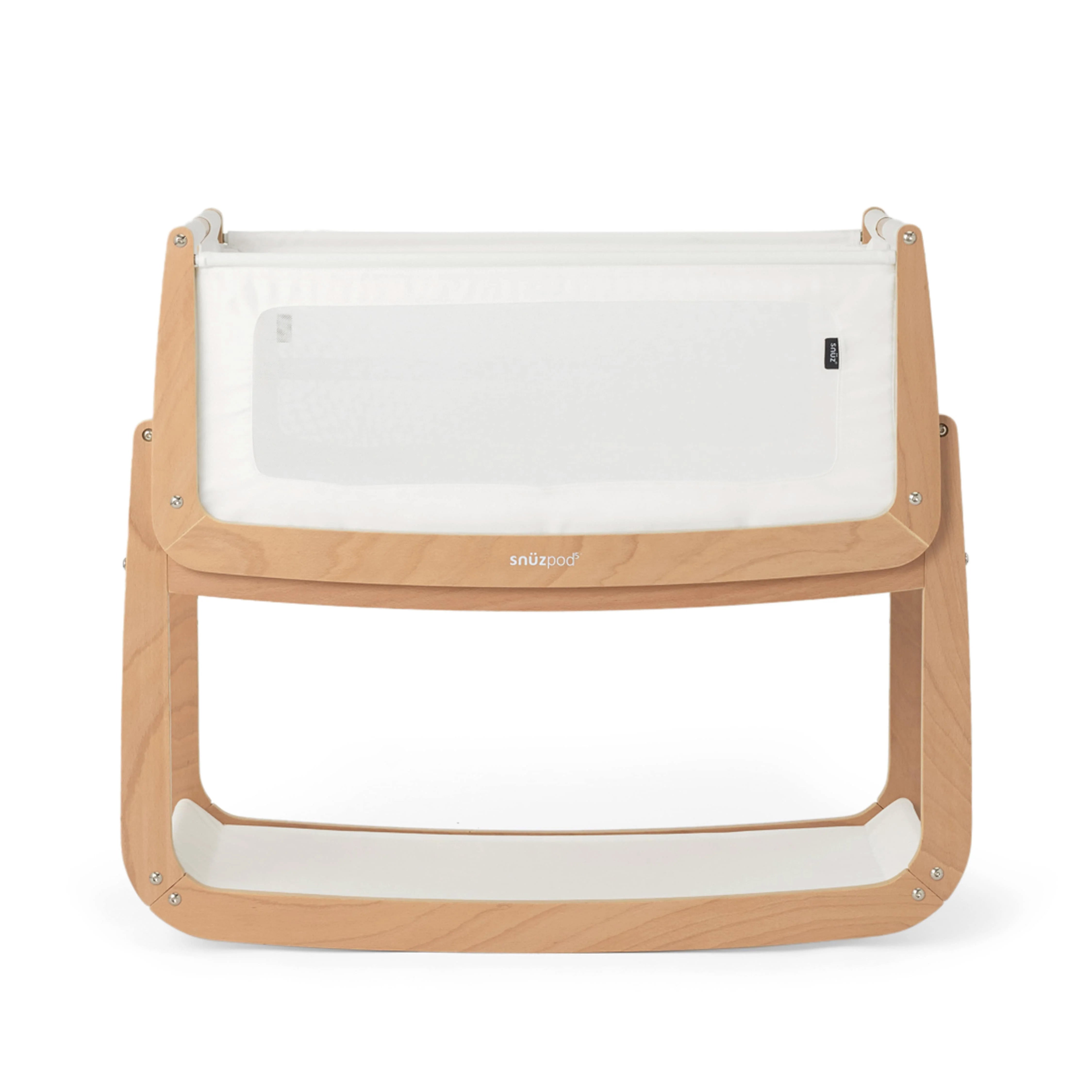 The SnuzPod5 bedside baby crib with a natural, unpainted wooden frame, white mesh sides, and a white mattress. 