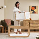 A woman detaching the SnuzPod5 bassinet from the main rocking frame, showing how easily portable this baby cot is.