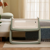 The SnuzPod 5 bedside baby crib with a lovely sage green wooden frame, next to an adult's bed in a beautifully decorated bedroom.